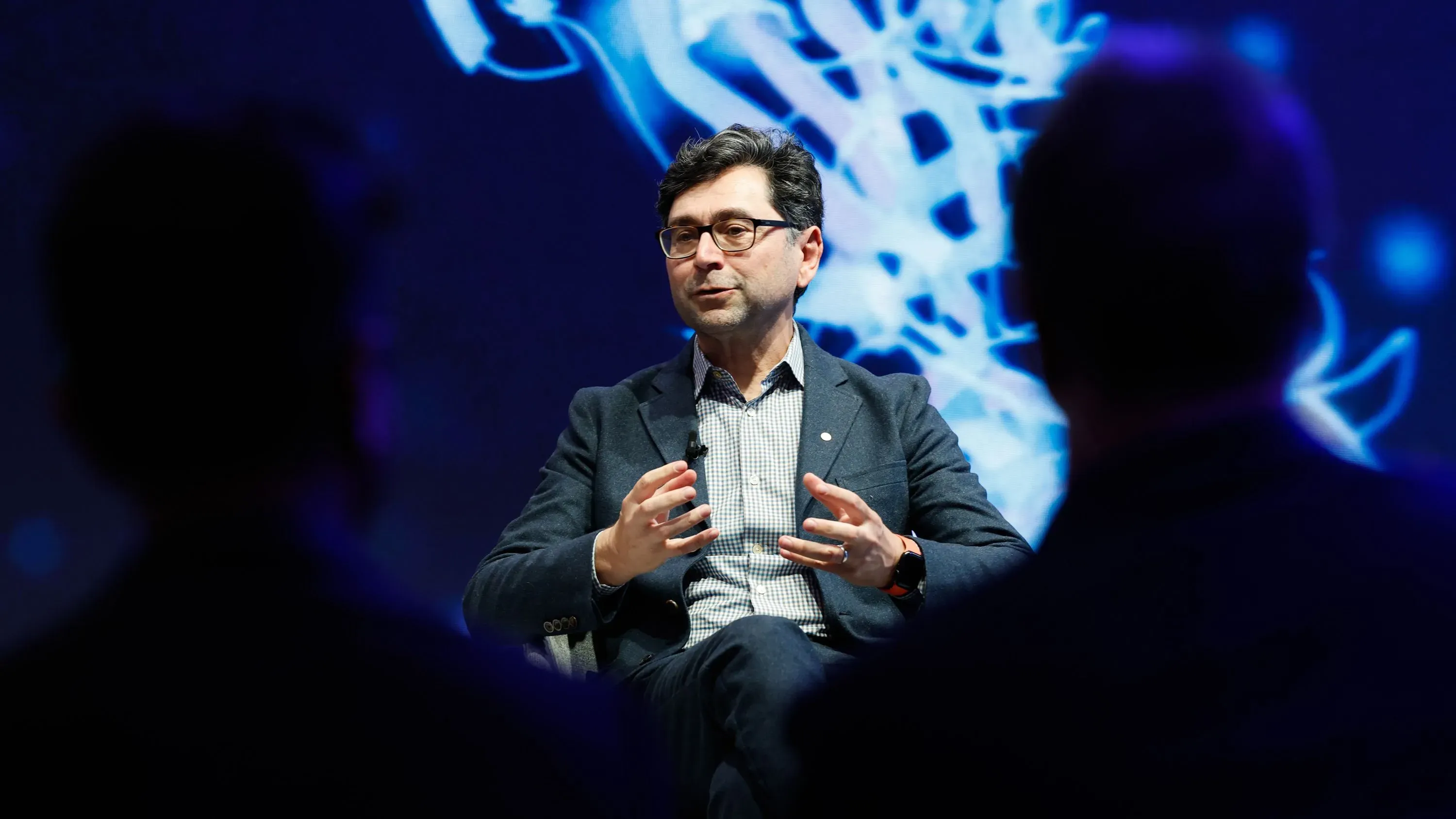 عالم يتحدث في مؤتمر حول الأبحاث الطبية الحيوية، مع خلفية تعرض رسومات علمية، مما يعكس أهمية الابتكار في هذا المجال.