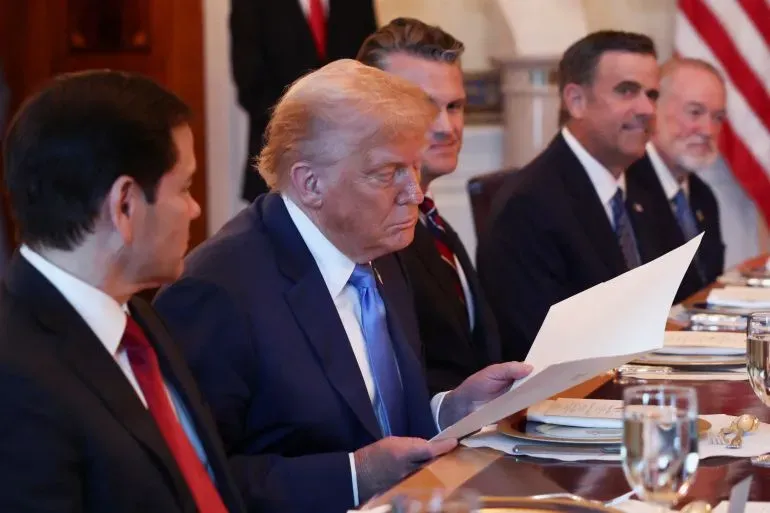 تظهر الصورة الرئيس الأمريكي دونالد ترامب وهو يتصفح ورقة خلال اجتماع رسمي، محاطًا بمستشارين. تعكس الصورة أجواء الترقب حول جوائز نوبل.