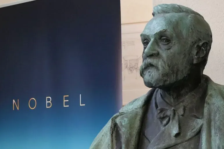 تمثال برونزي لألفريد نوبل، مع خلفية تحمل اسم "نوبل"، يرمز إلى جوائز نوبل في العلوم والطب.