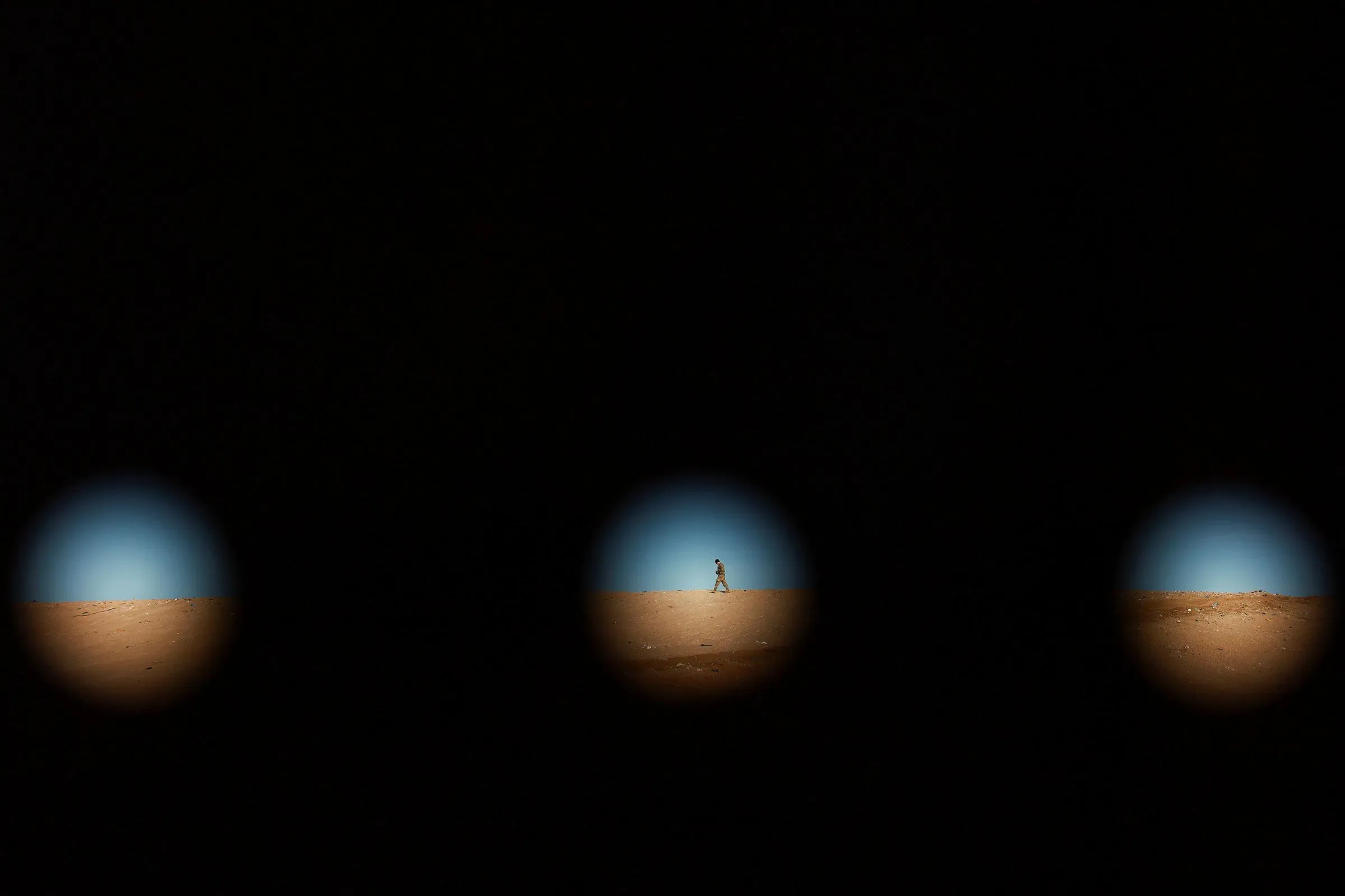 رجل يسير في صحراء تحت سماء زرقاء، يظهر من خلال ثلاث فتحات داكنة، مما يرمز إلى قضايا الهجرة والتحديات السياسية.