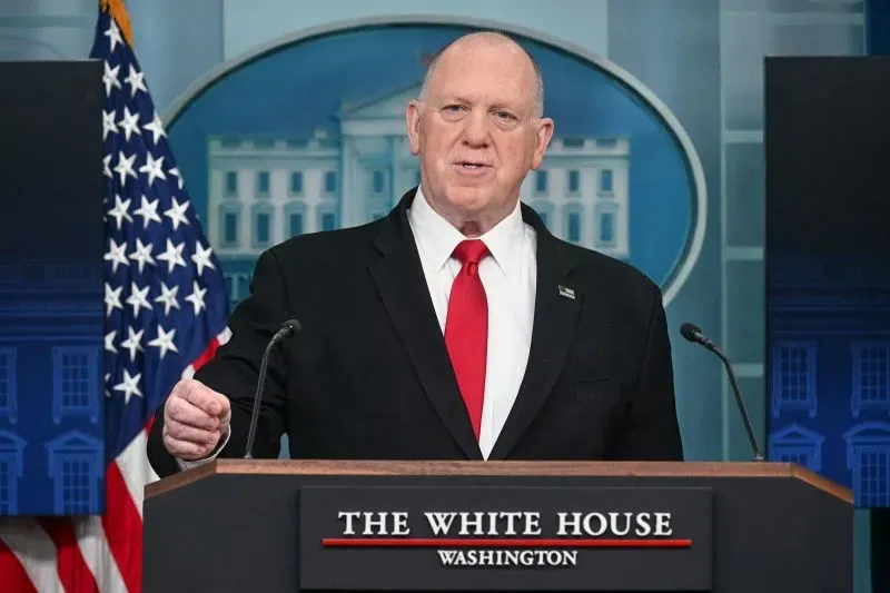 رجل يرتدي بدلة سوداء وقميص أبيض وربطة عنق حمراء، يتحدث في مؤتمر صحفي بالبيت الأبيض، مع العلم الأمريكي خلفه.