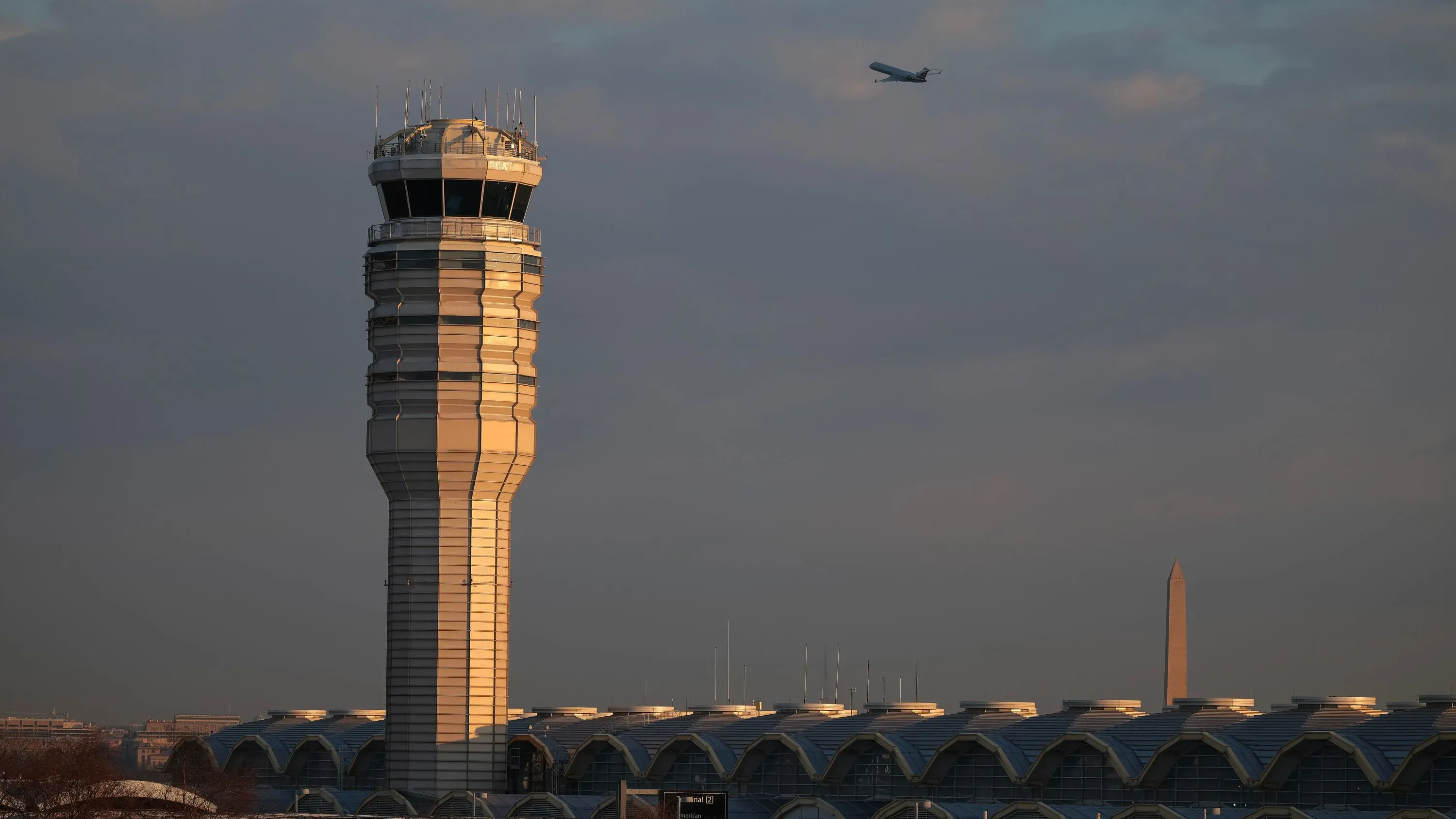 برج المراقبة في مطار ريغان الوطني مع طائرة تحلق في السماء، خلفه نصب واشنطن، في سياق تحقيق حول هبوط غير مكتمل لرحلات تجارية.