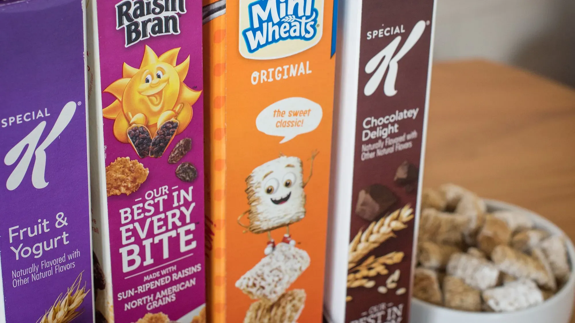 عبوات حبوب الإفطار الشهيرة "رايزن بران" و"ميني ويتس" و"تشوكليت ديلايت" من شركة WK Kellogg، مع وعاء من الحبوب في الخلفية.