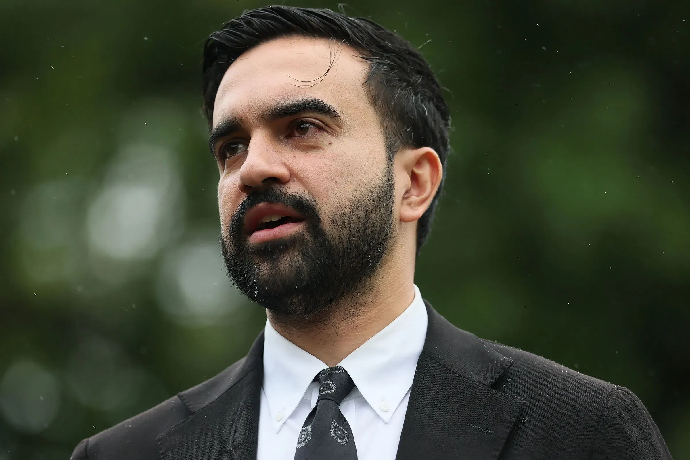 شخص يتحدث في مؤتمر صحفي، مع خلفية طبيعية، يعبر عن موقفه من الانتخابات والمنافسة السياسية في نيويورك.