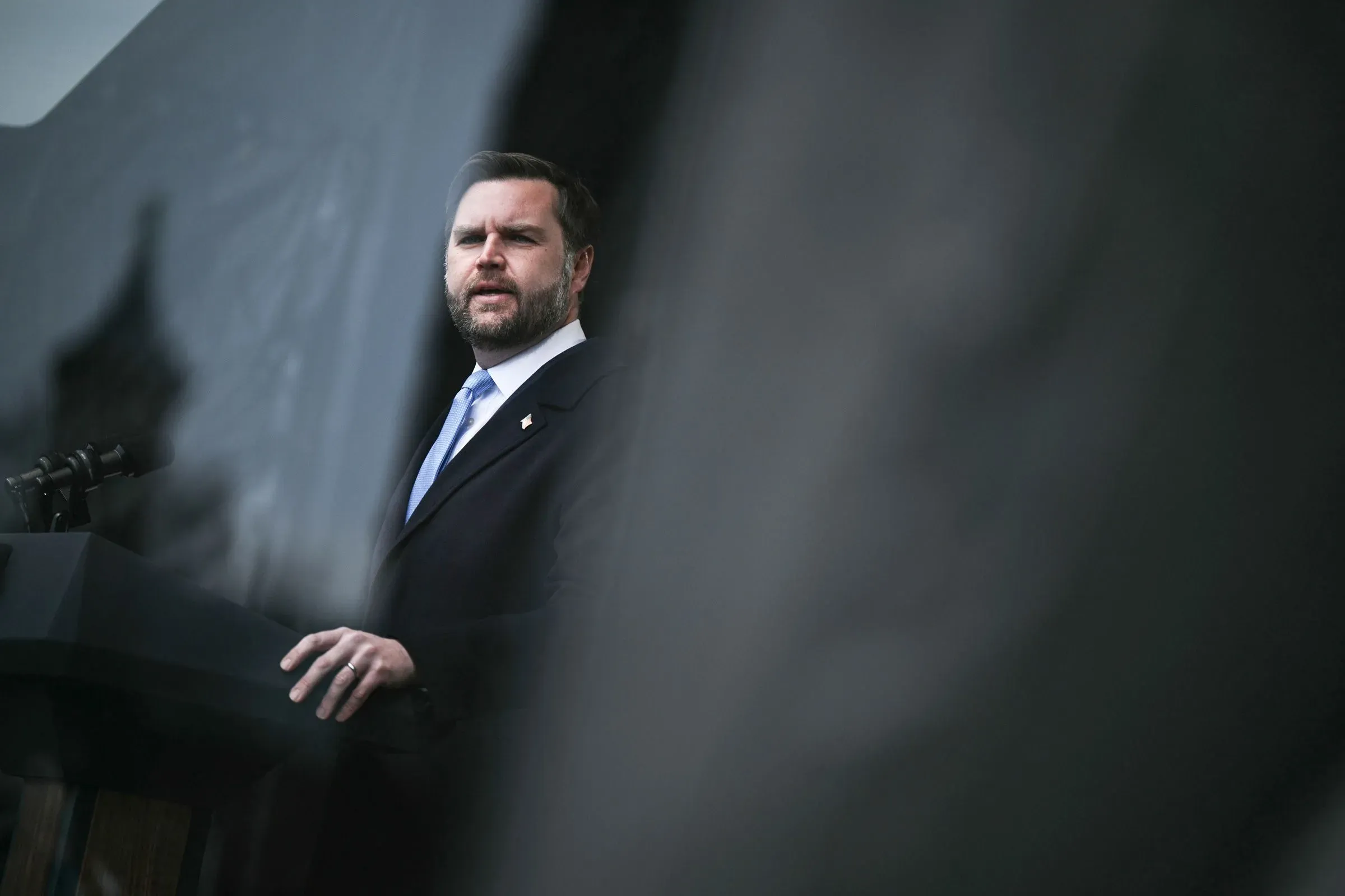 تظهر الصورة جيه دي فانس، نائب الرئيس الأمريكي، خلال خطاب رسمي، مع التركيز على تعبير وجهه الجاد في سياق تهديدات العنف السياسي.