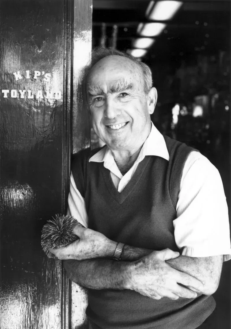 صورة لدون كيبر، صاحب متجر كيبز توي لاند، يقف مبتسمًا أمام مدخل المتجر، ممسكًا بلعبة، مما يعكس تاريخ المتجر العريق في بيع الألعاب.