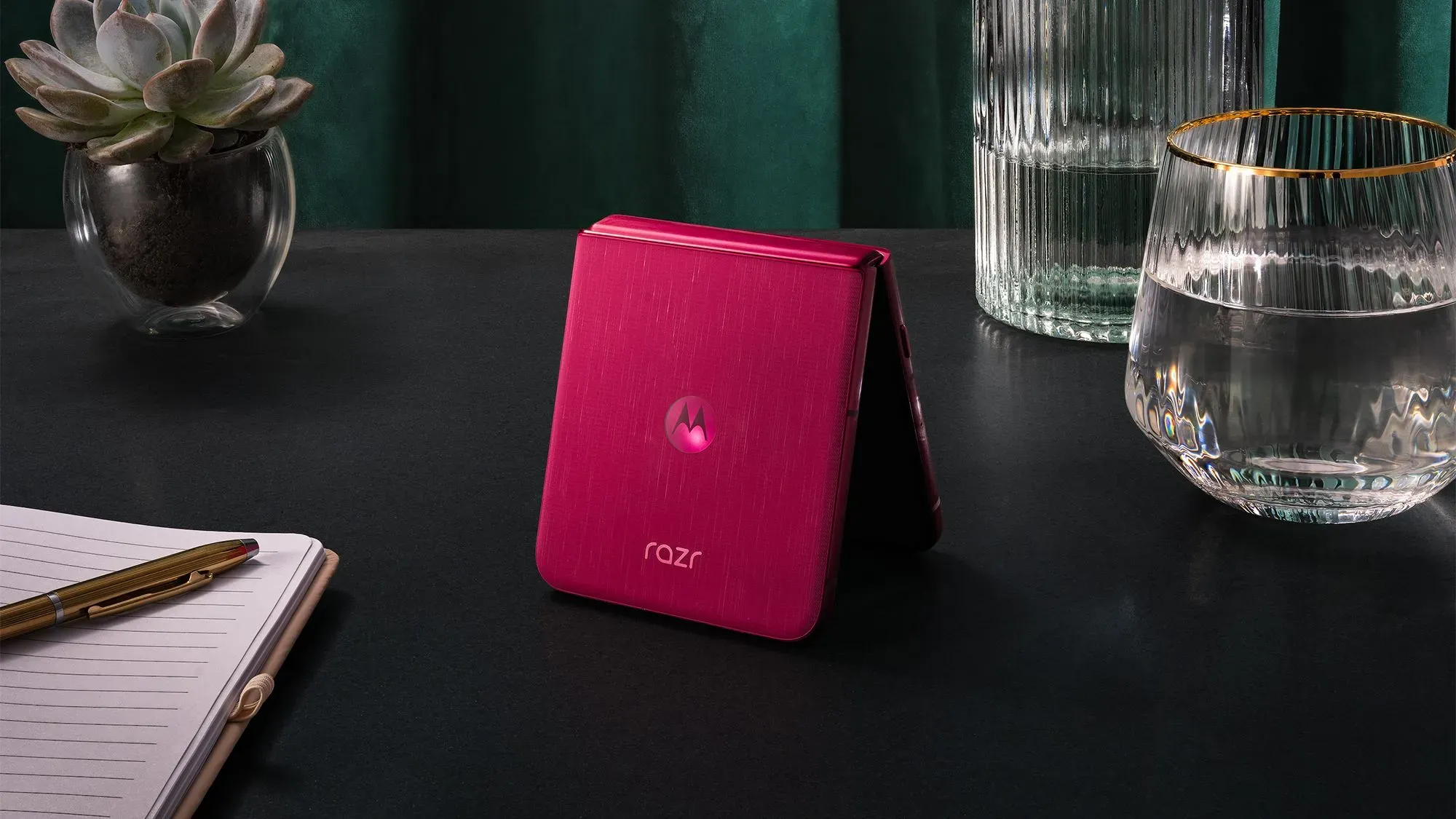 هاتف موتورولا Razr القابل للطي باللون الوردي، موضوع على طاولة بجانب نبات وزجاجتين، يمثل الجيل الجديد المدعوم بالذكاء الاصطناعي.