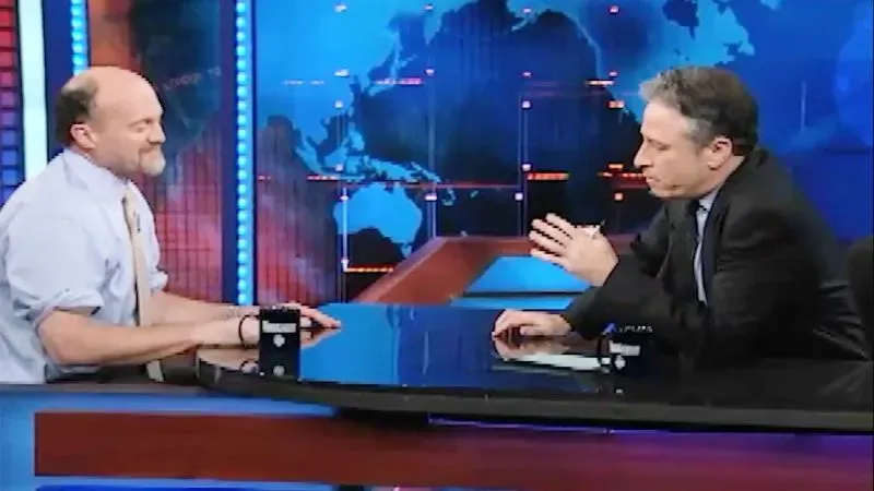 مقابلة بين جيم كرامر وجون ستيوارت على منصة تلفزيونية، حيث يناقشان موضوعات اقتصادية واجتماعية في سياق الفكاهة.