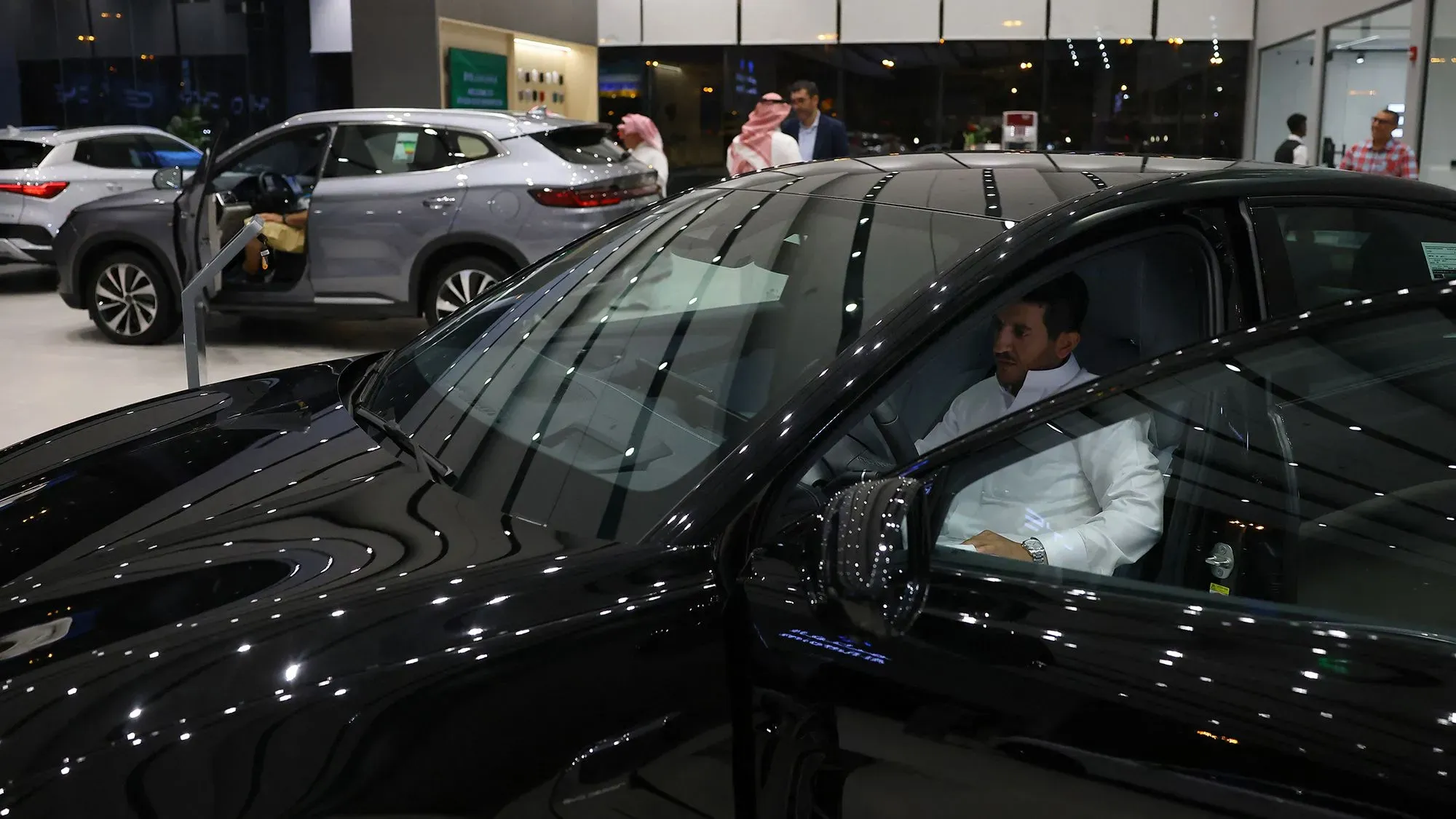 رجل يجلس داخل سيارة كهربائية في صالة عرض، مع سيارات كهربائية أخرى في الخلفية، مما يعكس تحول سوق السيارات في السعودية.