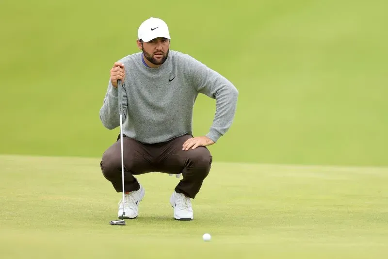 لاعب غولف يتأمل في وضعية الانطلاق، يرتدي ملابس رياضية، مع ملعب أخضر في الخلفية، وسط أجواء ممطرة أثناء بطولة أيرلندا الشمالية المفتوحة.