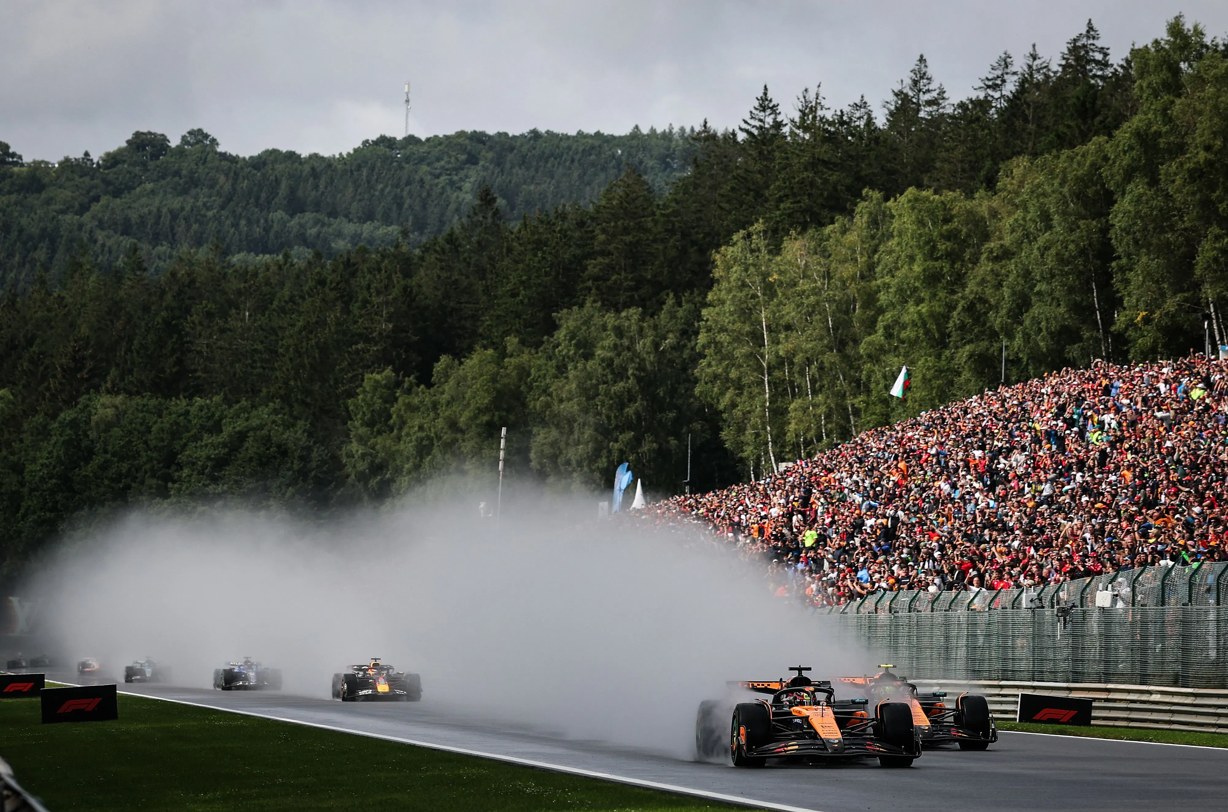 سيارات الفورمولا واحد تتسابق على حلبة سبا-فرانكورشان تحت المطر، مع ظهور سحب من الماء خلفها وجمهور كبير يتابع السباق.