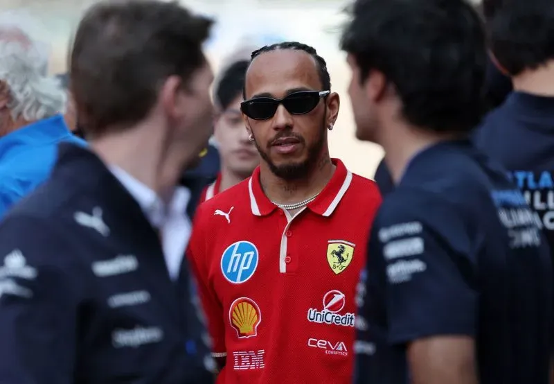 لويس هاميلتون يرتدي زي فيراري الأحمر ونظارات شمسية، يتحدث مع زملائه في سباق الجائزة الكبرى الصيني.