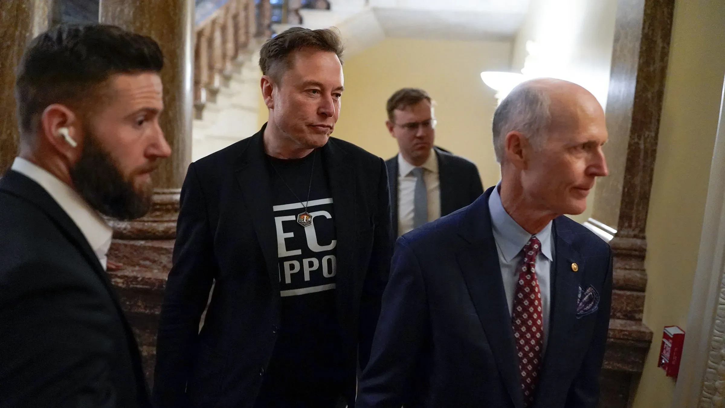 إيلون ماسك يتحدث مع المشرعين في الكابيتول هيل، محاطًا بحراسه الشخصيين، في سياق مناقشات حول برامج الفيدرالية.