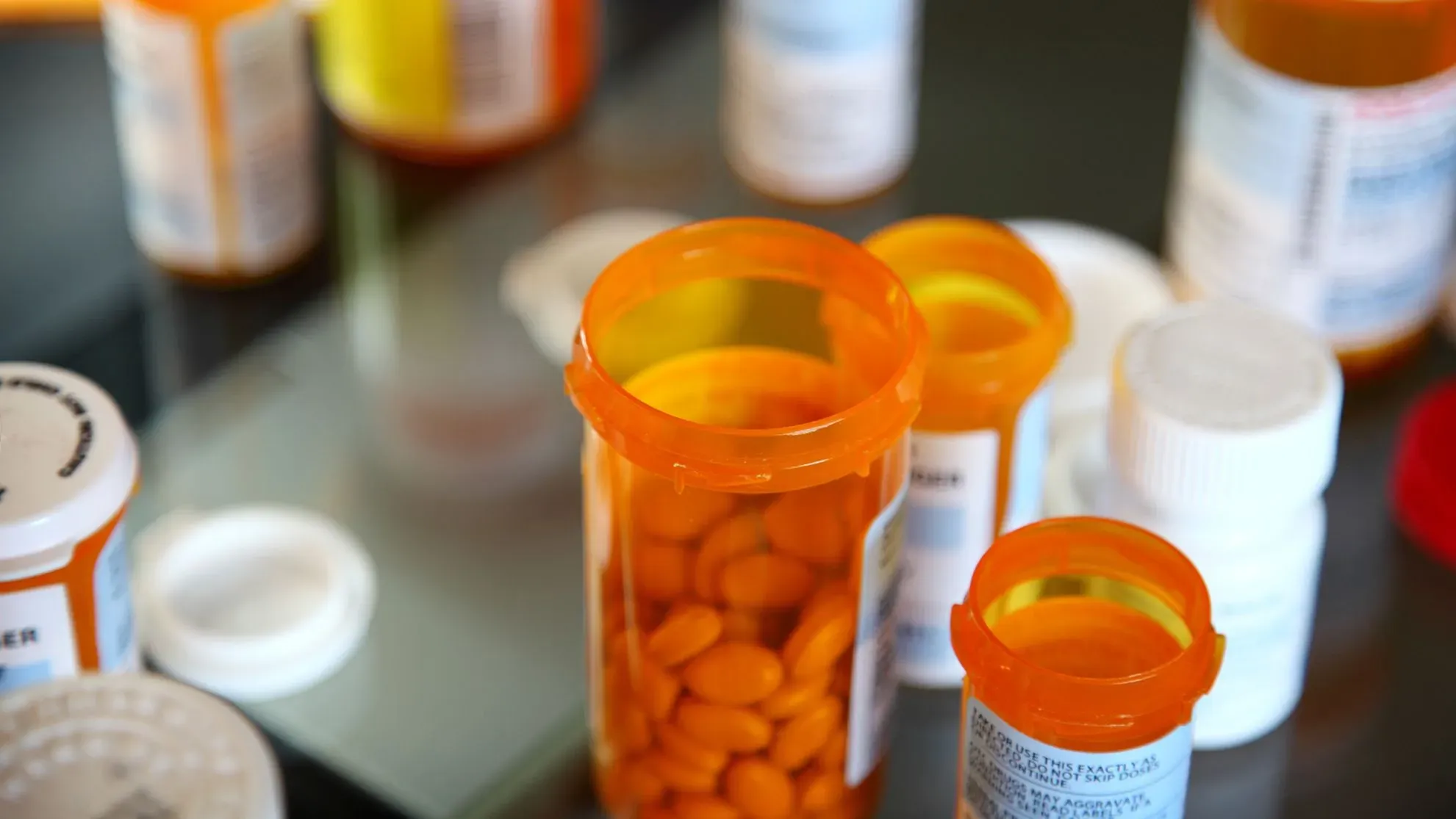 زجاجات دواء ملونة، مع التركيز على زجاجة برتقالية تحتوي على حبوب، تعكس موضوع مفاوضات أسعار الأدوية في برنامج Medicare.