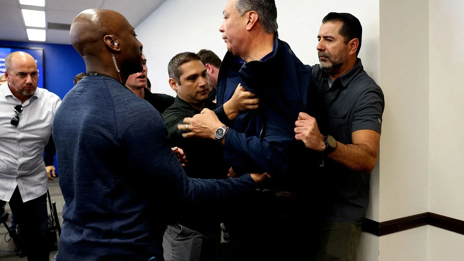 اشتباك بين عدة أشخاص خلال حدث عام، حيث يظهر أحدهم محتجزًا بينما يحاول الآخرون التدخل، مما يعكس التوترات السياسية الحالية.