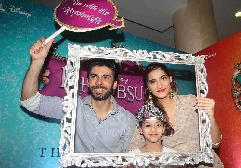 فواد خان مع ممثلة وطفلة، يحتفلون في فعالية ترويجية لفيلم، مع خلفية ملونة تعكس أجواء السينما الهندية.