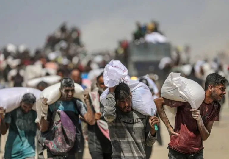 رجال يحملون أكياس مساعدات غذائية في غزة، وسط تجمع كبير للناس، في ظل أزمة إنسانية متفاقمة بسبب الحصار والعمليات العسكرية.