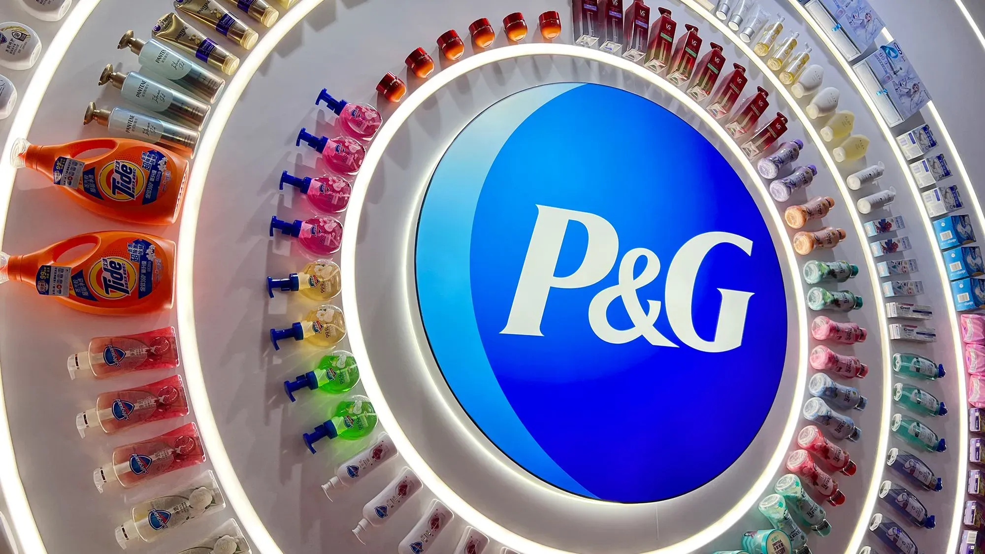 شعار شركة بروكتر آند جامبل مع مجموعة متنوعة من منتجات العناية المنزلية والشخصية، يعكس استراتيجية إعادة الهيكلة لمواجهة تحديات السوق.