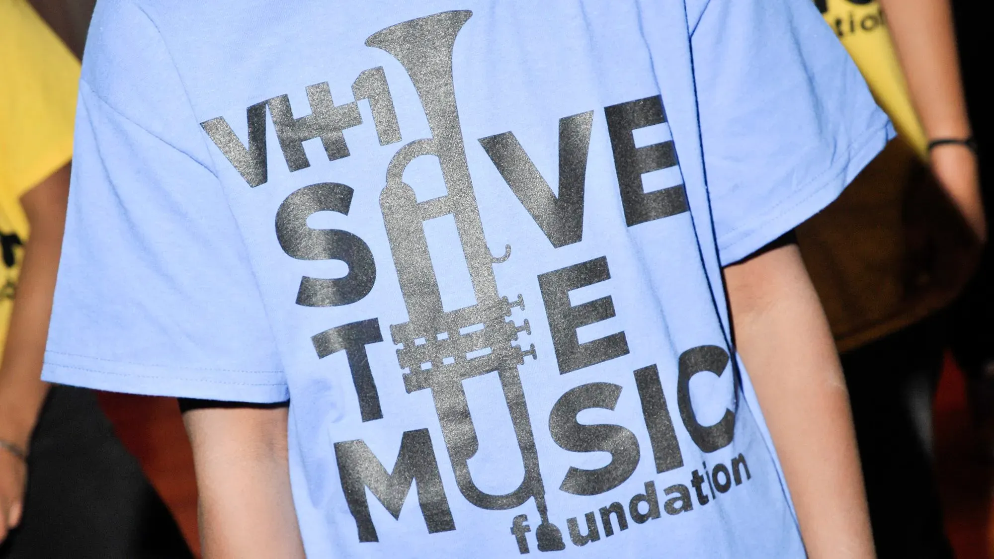 تيشيرت أزرق يحمل شعار "Save the Music" مع تصميم يبرز أداة موسيقية، يرمز لدعم التعليم الموسيقي في المدارس.