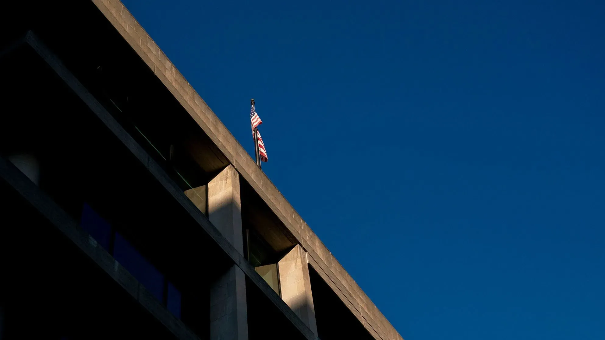 علم أمريكي يرفرف فوق مبنى حكومي، يعكس القلق المتزايد بين الموظفين الفيدراليين بشأن المراقبة في ظل إدارة ترامب.