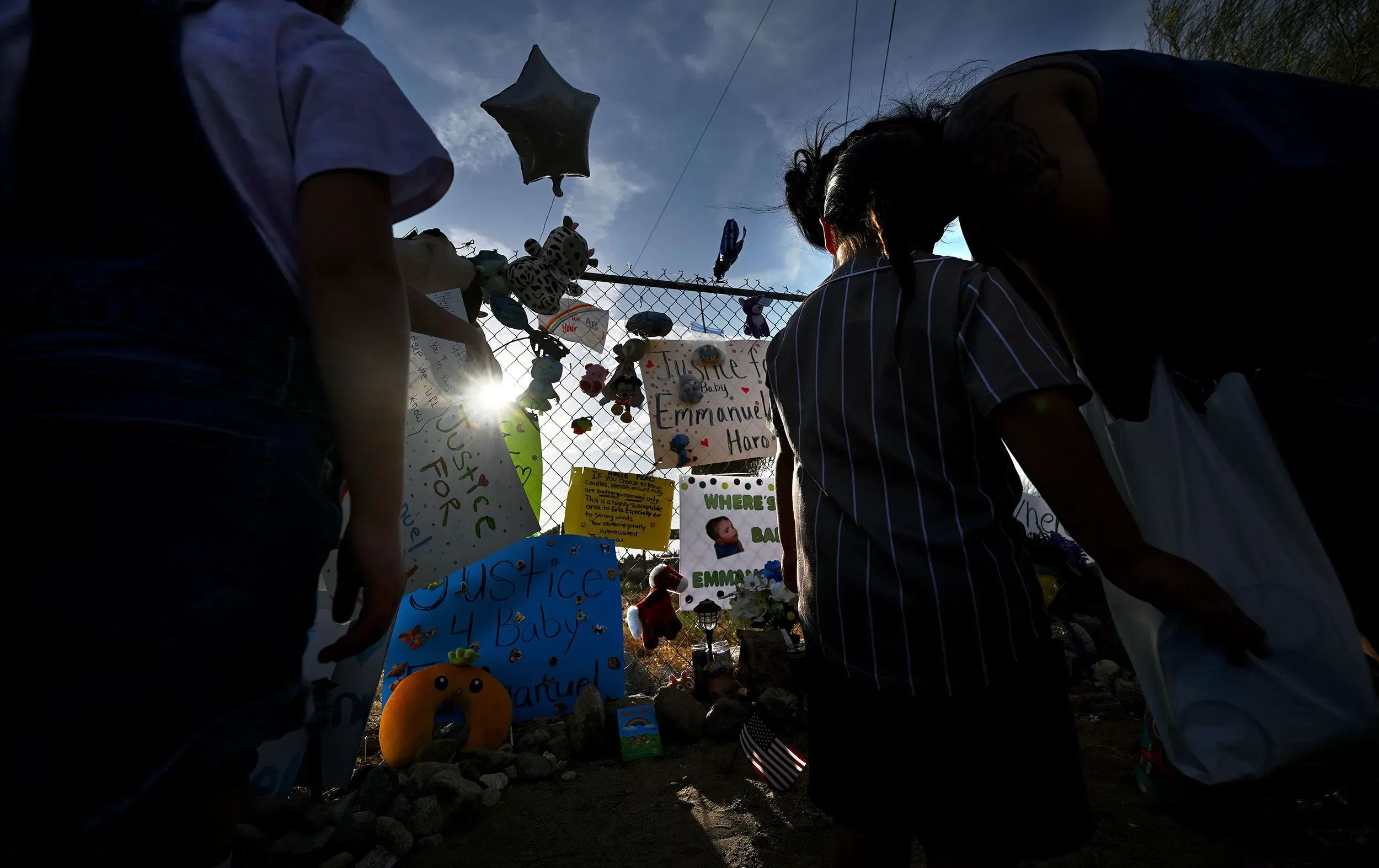 محتجون يقفون أمام نصب تذكاري لطفل مفقود، يحملون لافتات تطالب بالعدالة لإيمانويل هارو، مع أضواء ونجوم تتلألأ في الخلفية.