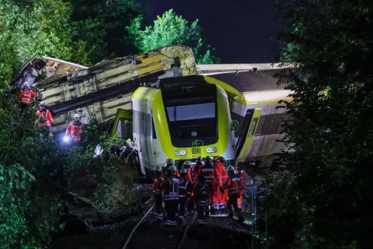 حادث قطار في ألمانيا يظهر عربات ملقاة على الجانبين، مع فرق الطوارئ تعمل على إنقاذ الركاب المصابين.