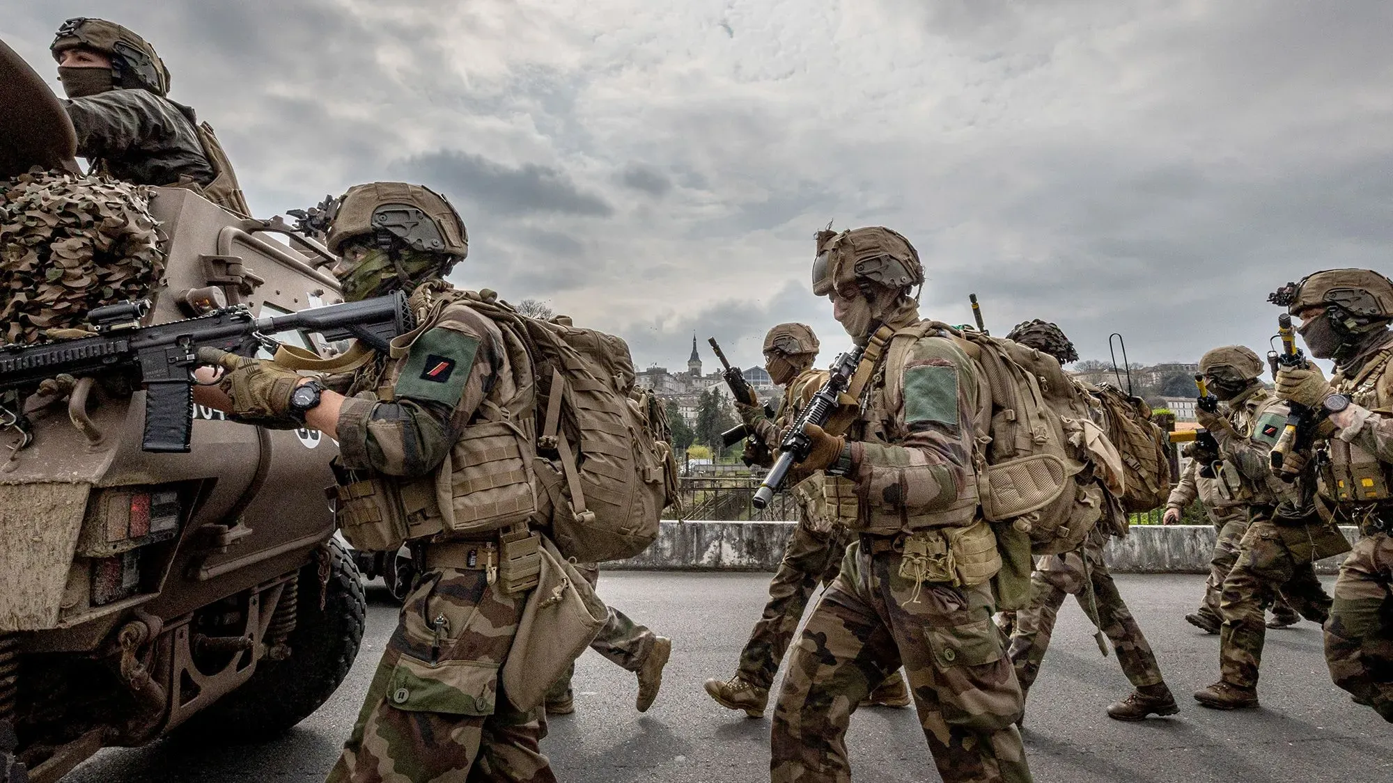 جنود يرتدون زيًا عسكريًا ويحملون أسلحة، يسيرون في صف أمام مركبة عسكرية، في مشهد يعكس تعزيز الدفاع الأوروبي في ظل التوترات الجيوسياسية.