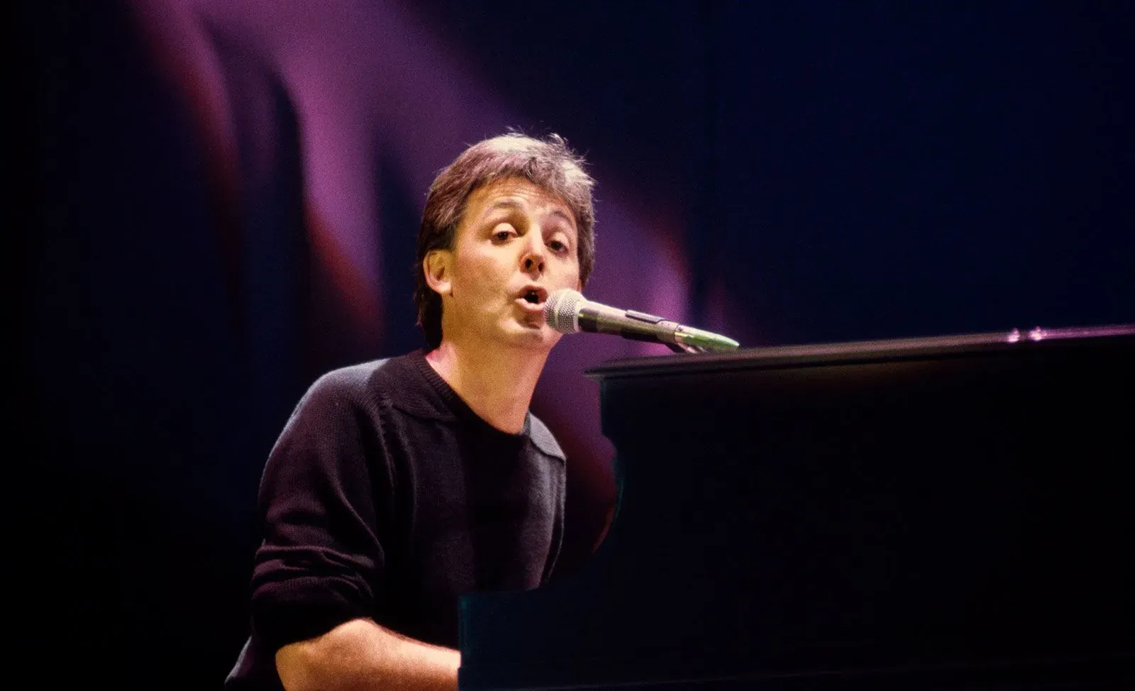 بول مكارتني يغني "Let It Be" على البيانو في حفل Live Aid عام 1985، وسط أضواء المسرح والجمهور.