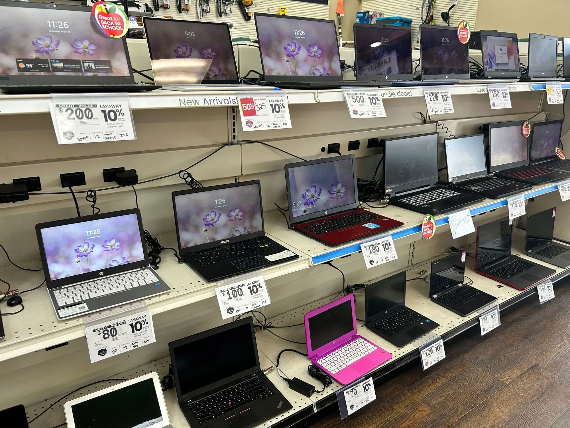 أجهزة كمبيوتر محمولة معروضة على رف في متجر رهن، مع ملصقات أسعار توضح التخفيضات، تعكس خيارات التسوق الاقتصادية لموسم العودة إلى المدرسة.