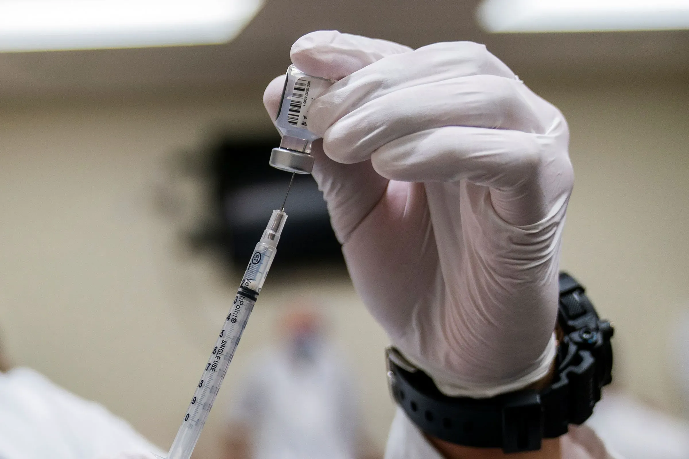 حقنة لقاح كوفيد-19 تُجهز للاستخدام، مع التركيز على الإبرة والزجاجة، في إطار جهود البنتاغون لإعادة الجنود المفصولين للخدمة.