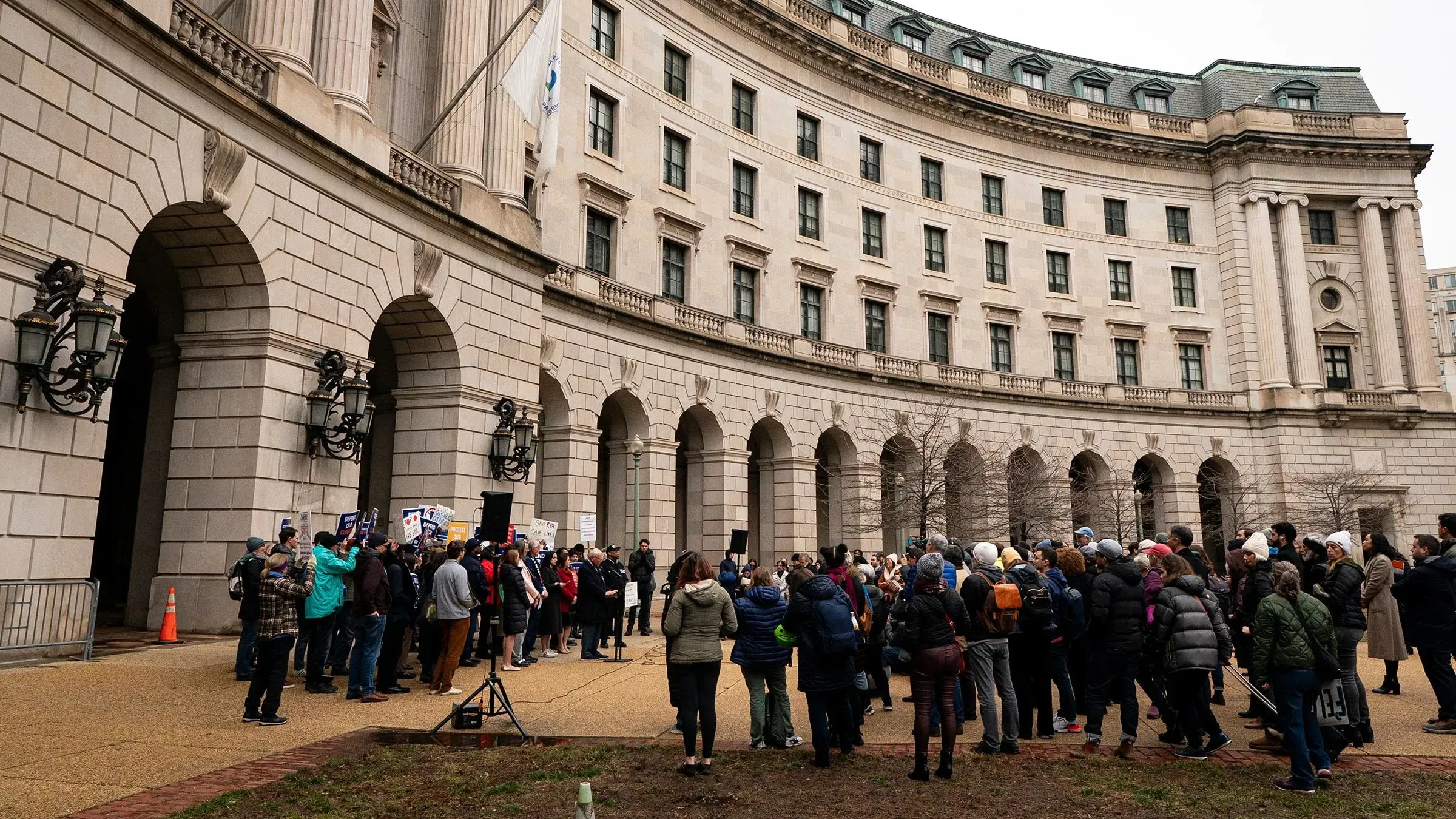 تجمع حشد كبير أمام مبنى وكالة حماية البيئة في واشنطن، مع لافتات تعبر عن القلق من تجميد التمويل الفيدرالي.