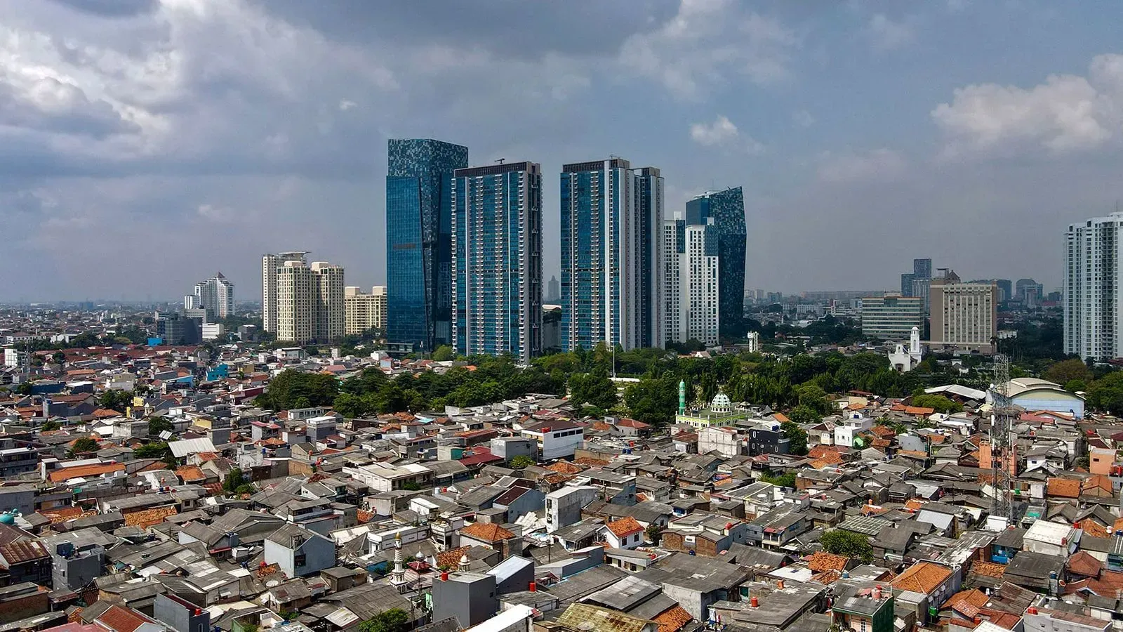 صورة تظهر تباين الحياة في إندونيسيا، حيث تتداخل المباني الحديثة مع الأحياء الفقيرة، مما يعكس موضوع الازدهار والسعادة.
