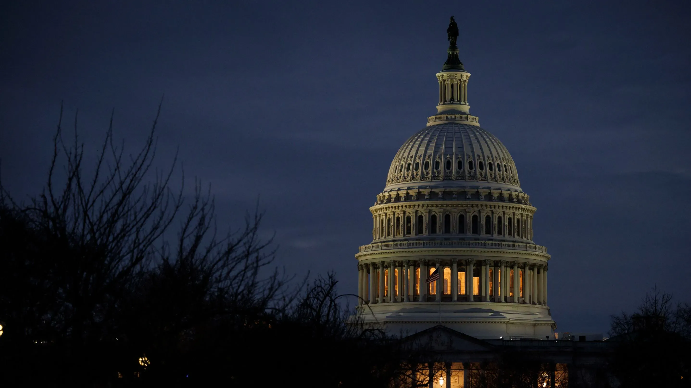 قبة مبنى الكابيتول الأمريكي مضاءة في المساء، محاطة بأشجار عارية، تعكس أهمية التعديلات الدستورية والنقاشات السياسية الجارية.