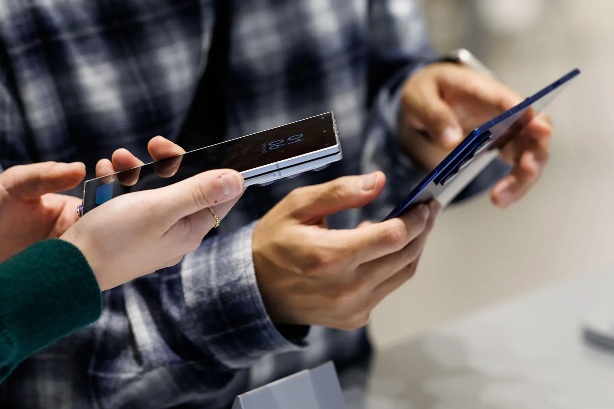 أشخاص يتبادلون الهواتف الذكية في متجر، مع التركيز على تفاصيل التصميم والتكنولوجيا الحديثة، في سياق ارتفاع أسعار الذاكرة وتأثيرها على السوق.