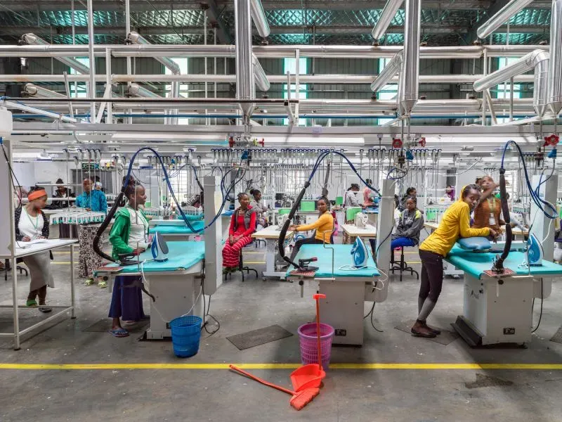 صورة تظهر عمالاً في مصنع، حيث يقومون بتشغيل آلات تصنيع الملابس. تعكس الصورة التحولات في سوق العمل العالمي وتأثير العولمة.