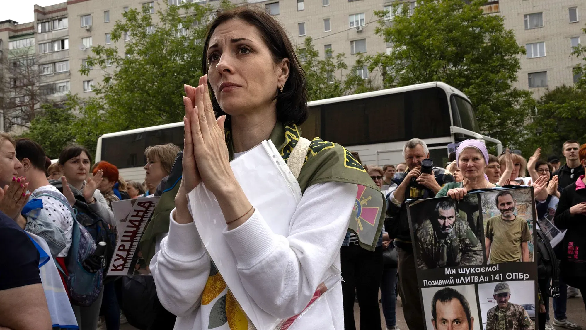 امرأة تحمل لافتة وتظهر تعابير القلق والأمل خلال تجمع لدعم أسرى الحرب الأوكرانيين، مع وجود حشد خلفها.