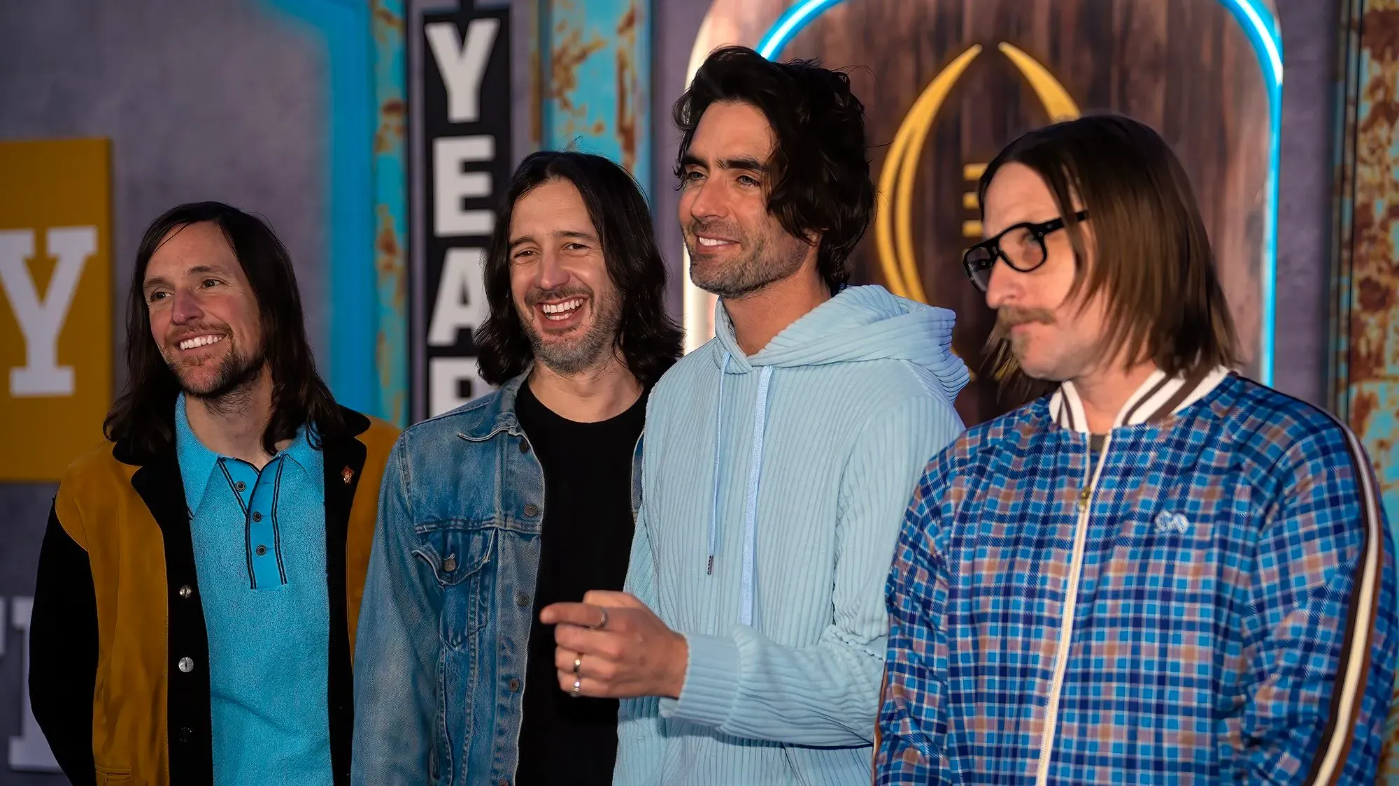 أعضاء فرقة The All-American Rejects يظهرون في حدث، مبتسمين ويتفاعلون مع الجمهور، مع خلفية ملونة تعكس أجواء موسيقى الإيمو.