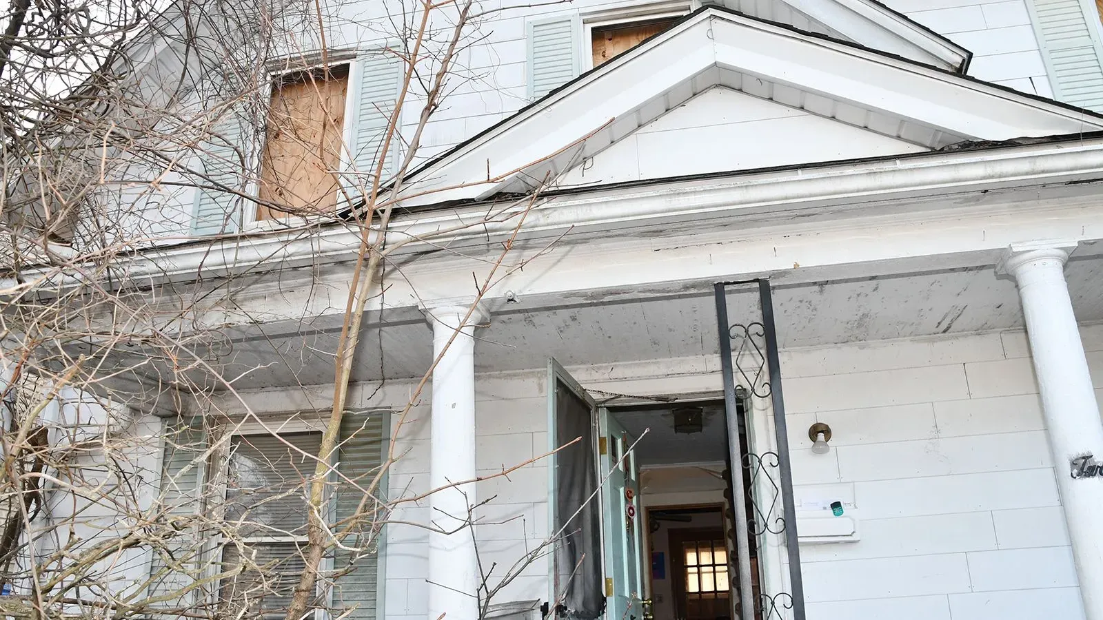 واجهة منزل مهجور في واتربري، كونيتيكت، تظهر علامات الإهمال، مع نوافذ مغطاة بالخشب الرقائقي وباب مفتوح، مما يعكس ظروف احتجاز قاسية.