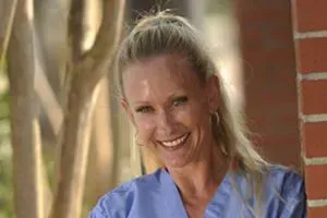 صورة لجولي جارد شنويل، أستاذة بيطرية متقاعدة، تظهر مبتسمة بزيها الطبي، مما يعكس شغفها بالتدريس ورعايتها للحيوانات.