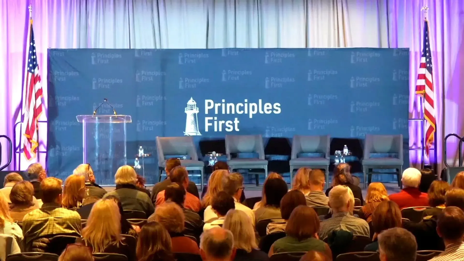 قاعة مؤتمر "المبادئ أولًا" في واشنطن، مع منصة فارغة وأعلام أمريكية، حيث تم إخلاء الحضور بسبب تهديدات أمنية.