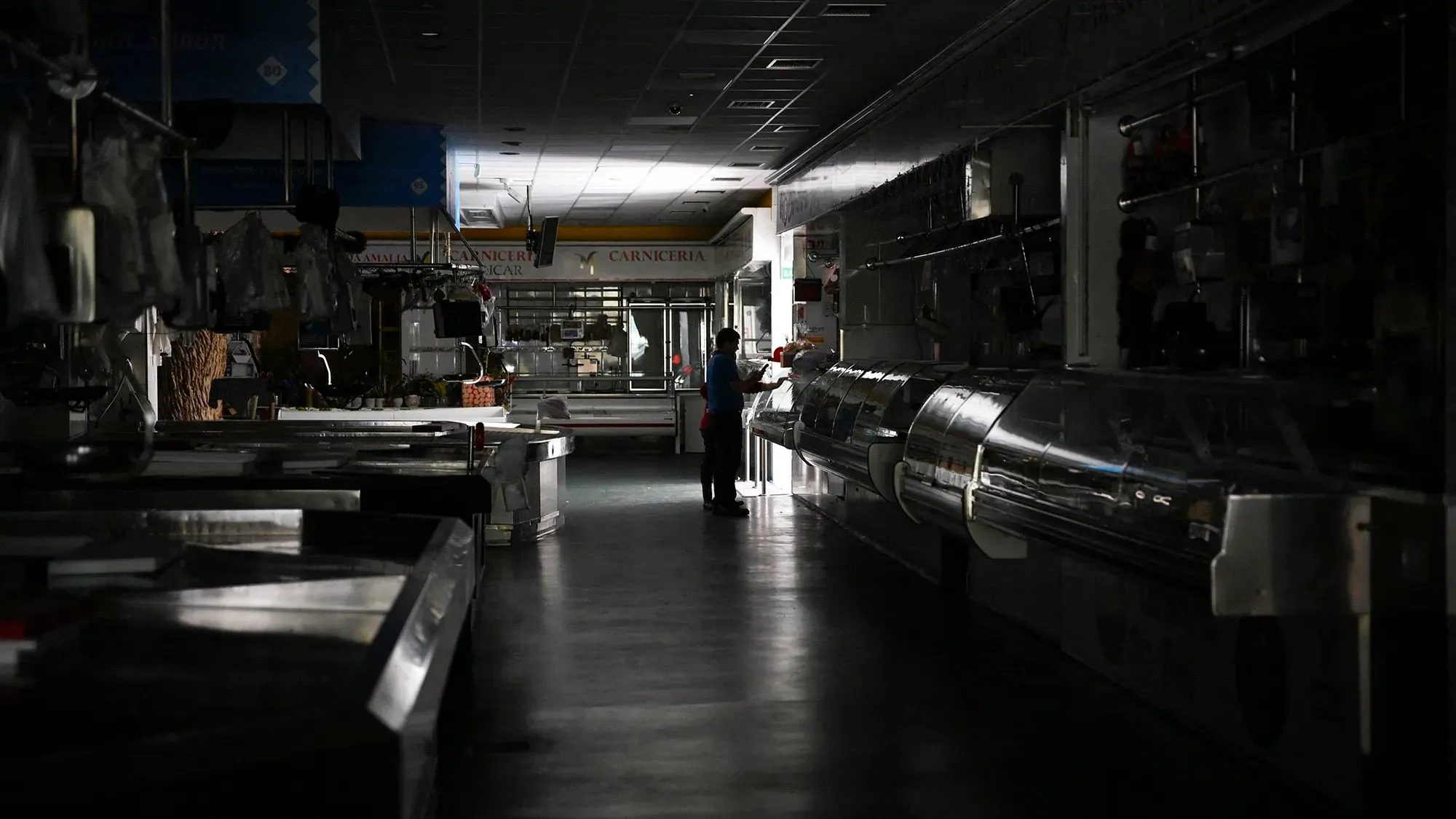 سوق مظلم بعد انقطاع التيار الكهربائي في إسبانيا، حيث يظهر شخص واحد في وسط المكان، مما يعكس تأثير انقطاع الكهرباء على الحياة اليومية.