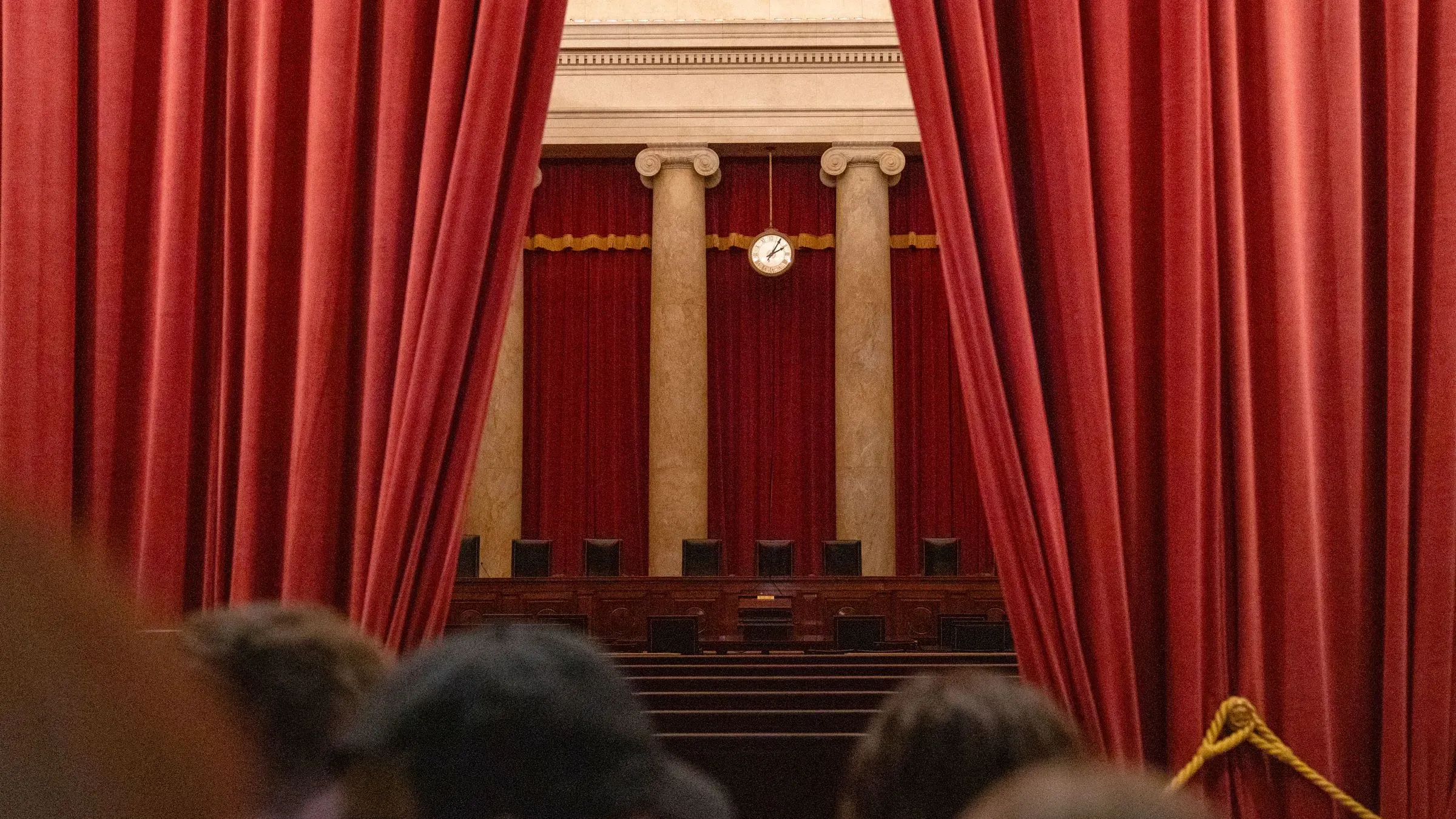 صورة لقاعة المحكمة العليا الأمريكية، تظهر ستائر حمراء وأعمدة، مما يعكس الأجواء الرسمية والتاريخية للمؤسسة القانونية في سياق التحديات القانونية الحالية.