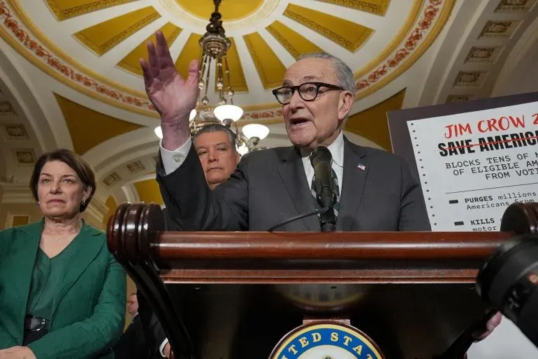 خطاب سياسي في الكونغرس الأمريكي، حيث يتحدث تشاك شومر مع أعضاء آخرين، مع لافتة تتعلق بقوانين التصويت.