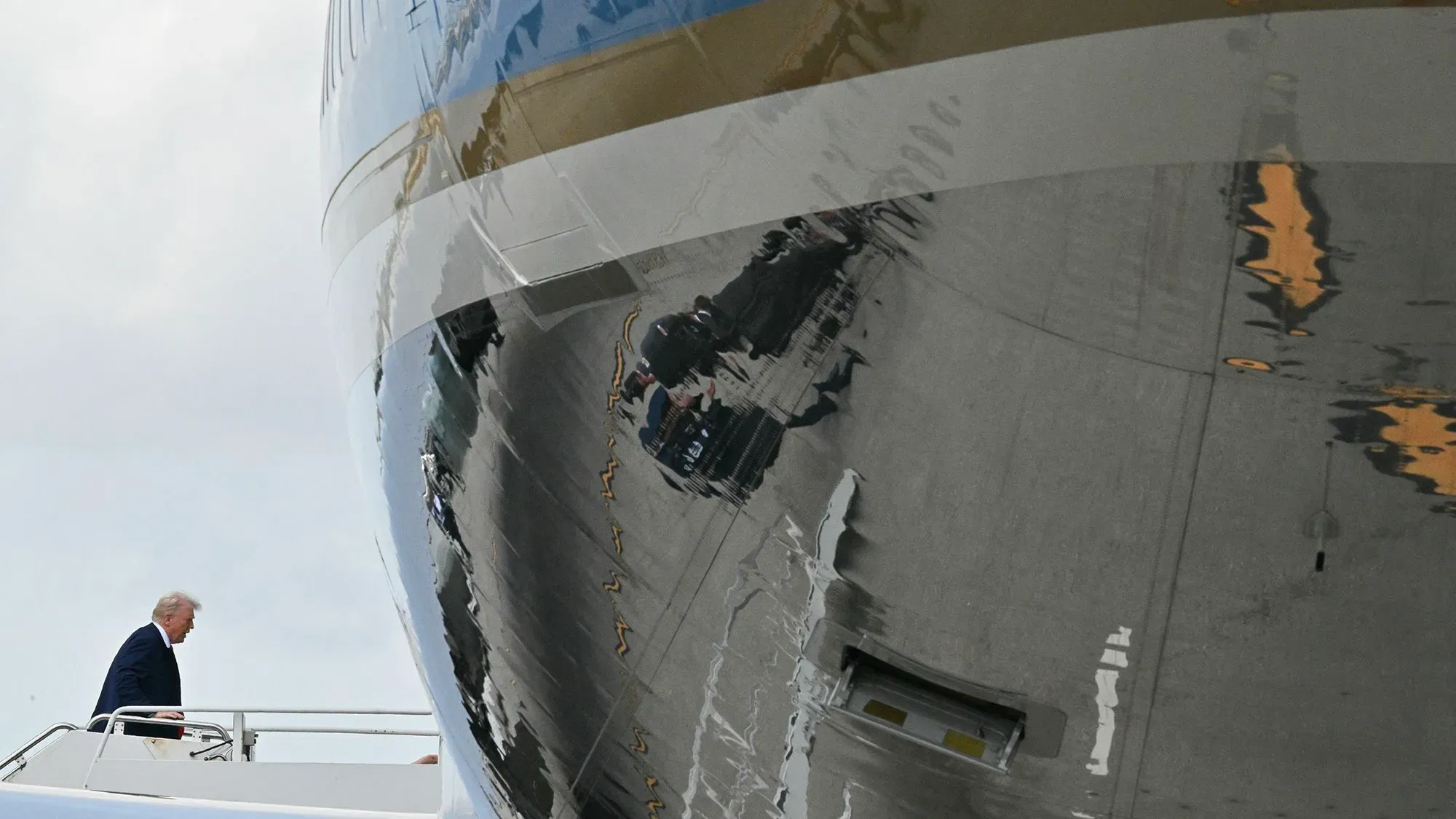 مقدمة الرئيس الأمريكي دونالد ترامب إلى طائرة إير فورس وان، مع انعكاس الطائرة على السطح المعدني، مما يعكس التوترات حول تأخيرات تسليمها.