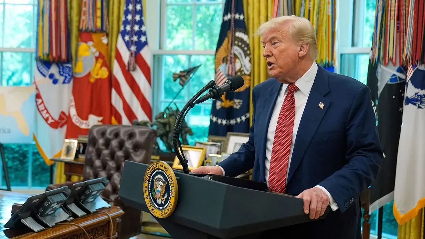 ترامب يتحدث في المكتب البيضاوي، محاطًا بالأعلام، حول صفقة تجارية محتملة مع دول كبرى، مع التركيز على تخفيف الرسوم الجمركية.