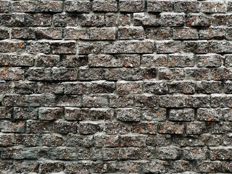 جدار من الطوب الرمادي مع تفاصيل خشنة وبقع ملونة، يعكس أسلوب ليو جياكون في التصميم المعماري المستدام والمستوحى من البيئة.