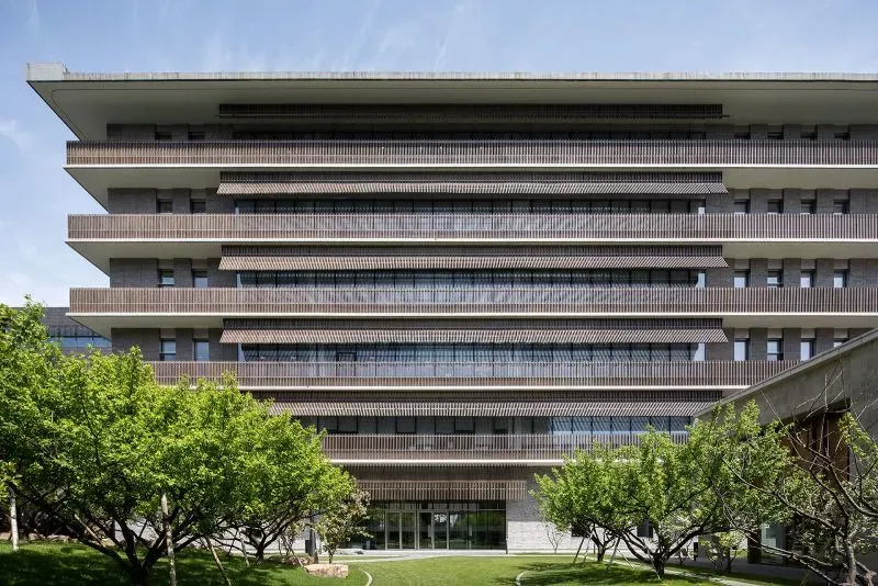 واجهة مبنى حديث بتصميم بسيط، يتكون من عدة طوابق مع شرفات، محاط بأشجار خضراء، يعكس أسلوب ليو جياكون في العمارة.