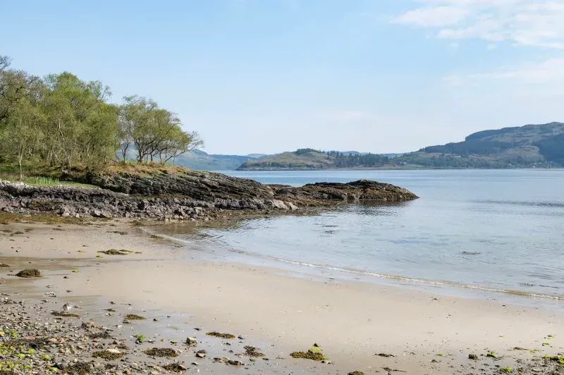 شواطئ جزيرة شونا الاسكتلندية، تُظهر المناظر الطبيعية الخلابة مع صخور ومياه هادئة، تعكس جمال الجزيرة المعروضة للبيع.