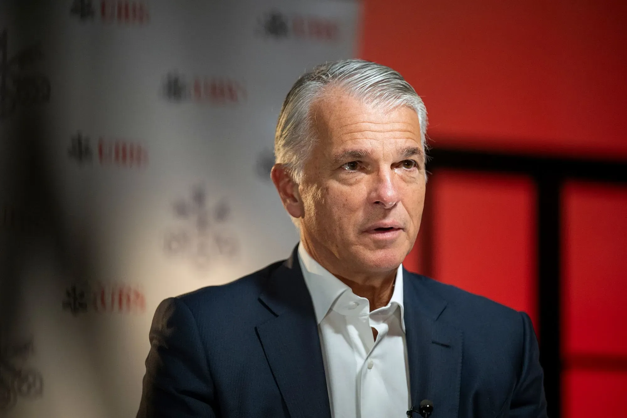 رئيس بنك يو بي إس يتحدث في مؤتمر، مع خلفية تحمل شعار البنك، حيث يتناول أداء البنك المالي والتحديات الاقتصادية.