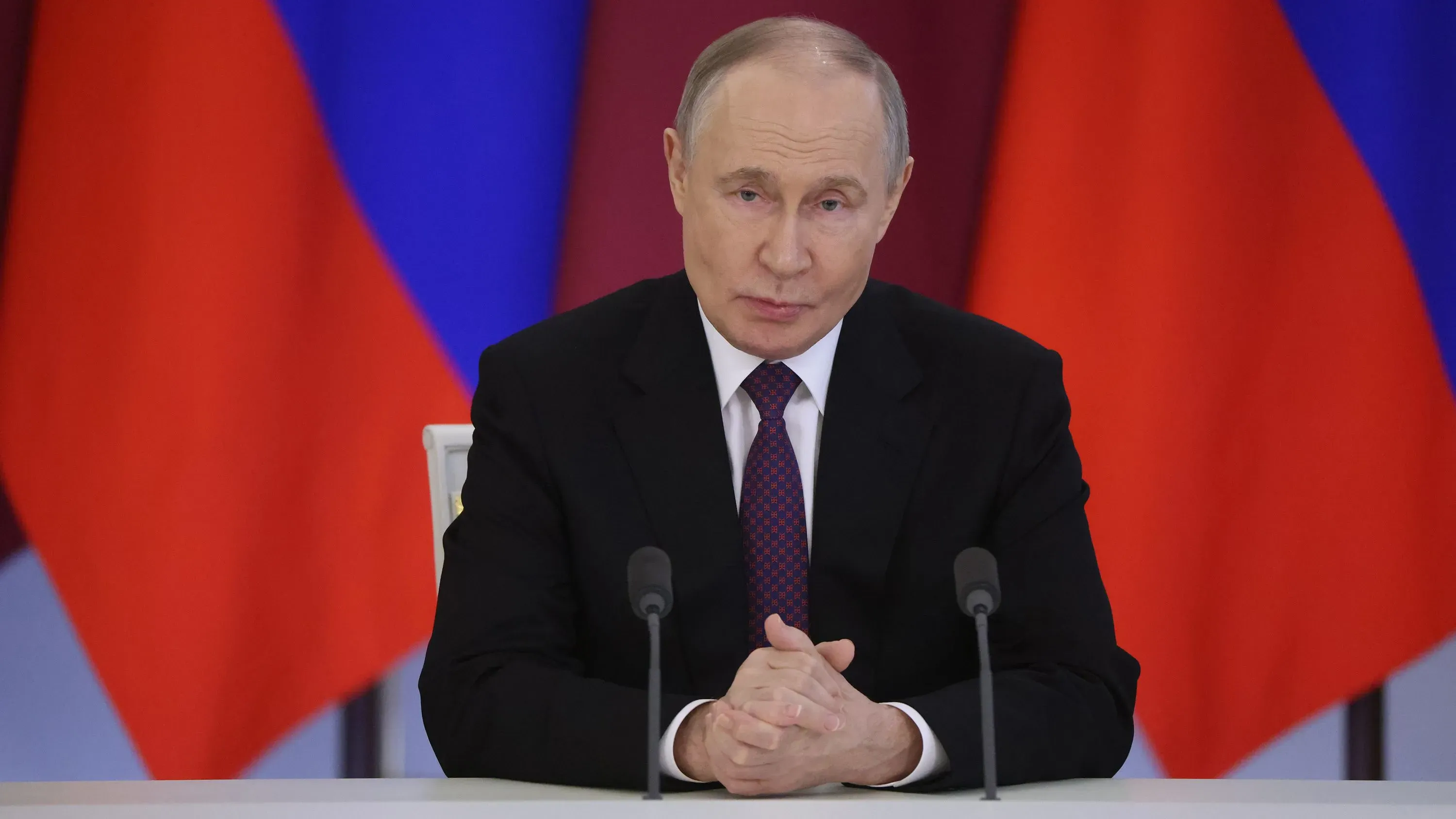 الرئيس الروسي فلاديمير بوتين يتحدث خلال مؤتمر صحفي، مع ظهور الأعلام الروسية خلفه، معلنًا عن وقف إطلاق النار في أوكرانيا.